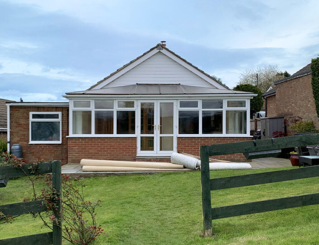 A conservatory with a tiled roof is attached to a brick building, viewed from across a green lawn.